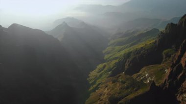 Yumuşak sisli güneşli yeşil vadi. Dağınık kır evleri ve dolambaçlı patikaları olan pastoral yamaçlar.