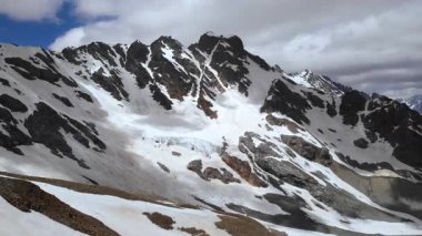 Bulutlarla süpürülmüş dağlık tepeler yamalı kar ve engebeli granit kuleler bulutlu gökyüzü ve şiddetli rüzgar yaratıyor. Medya