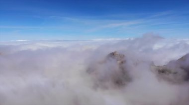 Kalın beyaz bulutların arasından görünen engebeli dağ zirvelerinin destansı hava görüntüleri. Medya