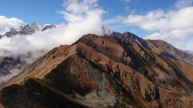 Manzaralı insansız hava aracı görüntüleri engebeli bir dağ sırasının üzerinde uçuyor. Tepelerin üzerinde bulutlar yüzüyor. Medya