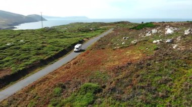 Güzel yeşil bir sahil şeridi boyunca dar bir yolda giden eğlence amaçlı bir aracın hava görüntüsü. Medya