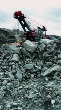 Hava manzaralı kayalık ön planda kaya ve molozlar, uzak kablo küreği ve çalışan kamyon var.