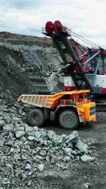 Hava manzaralı kazıcı taş ocağının kenarındaki taşıma kamyonuna kaya yığıyor, dik kenar ve gevşek moloz yığını, kapatın.