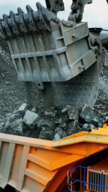 Hava manzaralı kova ağır kayayı nakliye kamyonuna boşaltıyor kova dişleri ve kamyon yatağının çerçevesini kapatıyor.