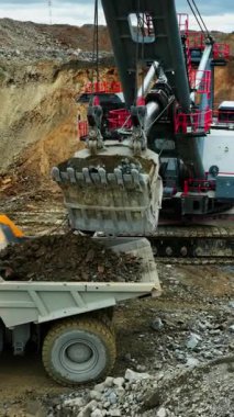 Yakın çekim kovası nakliye kamyonuna boşaltılıyor, ağır kayalar kamyon yatağına dökülüyor, dişler ve bağlantı görünüyor.,