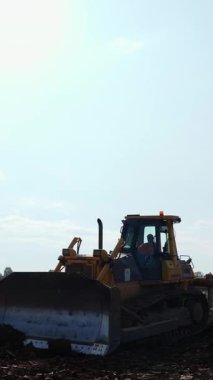 Buldozer güneşli bir günde inşaat alanında toprağı hareket ettiriyor. Kırp