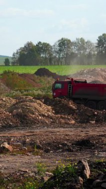 Kırmızı çöp kamyonu inşaat alanına toprak boşaltarak toz bulutu yaratıyor. Kırp