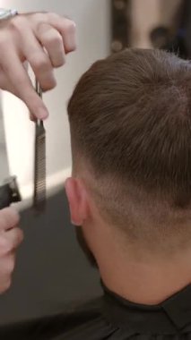 Erkek kuaför elektrikli makas ve tarak kullanarak müşteriye şık bir saç kesimi yapıyor. Kırp