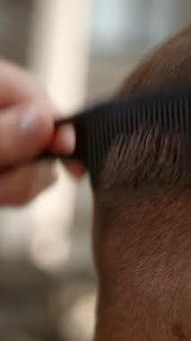 Bir müşteriye saç tıraşı yapmak için elektrikli tıraş makinesi ve tarak kullanan berber ellerini kapat. Kırp