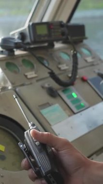 Üniformalı genç bir denizci bir teknede geziniyor ve kokpitteki el telsizine konuşuyor. Kırp