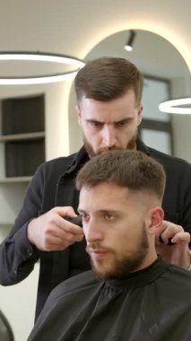 Modern bir berber dükkanında genç bir adamın saçını yapmak için elektrikli makas kullanıyor. Kırp