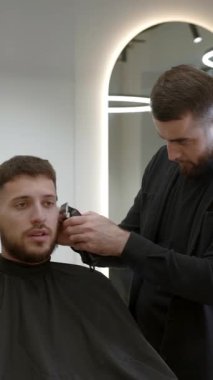 Çağdaş bir berber dükkanındaki kuaförden modern bir saç kesimi alan genç bir adam. Kırp