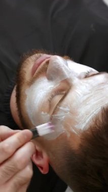 Güzellik uzmanı, güzellik salonundaki bir adamın yüzüne nemlendirici yüz maskesi uyguluyor. Kırp