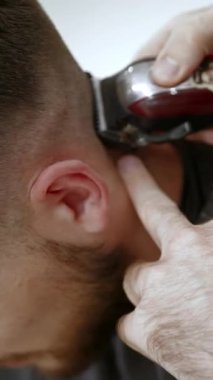 Bir berberin ellerini elektrikli jiletle yaka çizgisindeki bir müşterinin saçını budamak için kapat. Kırp