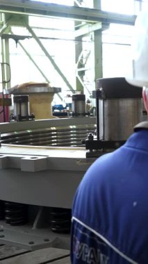 Fabrika işçisi büyük dairesel bir endüstriyel bölümü inceliyor ve notlar alıyor.