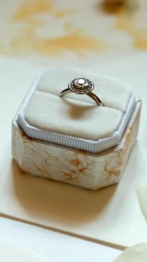 Beyaz arka plandaki açık kutusunda nergis ve düğün kırtasiyesiyle sergilenen incili alyans.