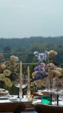 Çiçeklerle süslenmiş düğün masası ve renkli bardaklar güzel yeşil bir vadiye bakıyor.