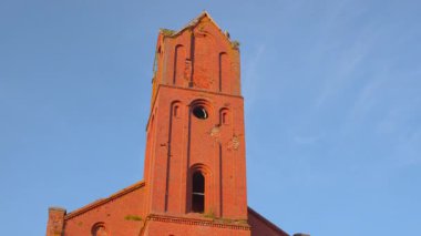 Açık Mavi Gök 'ün Altındaki Kırmızı Tuğla Kilise Kulesi, Güneş Işığı Yüzü, Uzun Çan Kulesi ve Yosun Yamaları. Medya