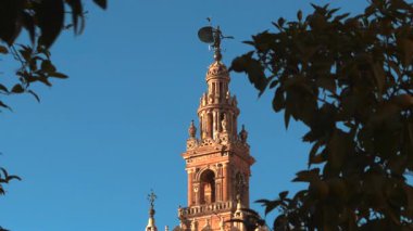 Terracotta Kulesi 'nin üzerinde rüzgar Vane' i var, yeşillik ve açık mavi gökyüzü çerçeveli, tuğla işçiliği ve sıcaklık karışıklığı. Eylem