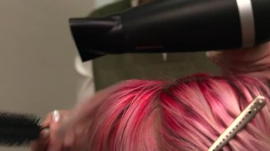 Stilist, pembe saç şekillendirmek için yuvarlak fırça ve kurutucu kullanıyor, kökleri yakın ısıtmalı başlık, çarpışma bölümleri. Medya