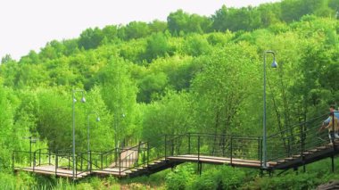 Green Hills 'in karşısındaki yüksek tahta geçitten geçen aylaklar, viraj yolu ve lamba direkleri peyzajı. Kırp