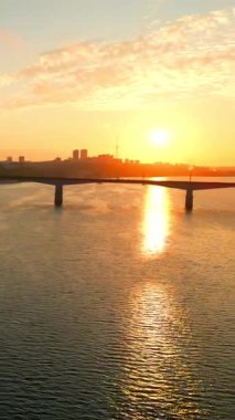 Turuncu güneş su yüzeyine yansıyor. Feribot nehir kıyısında yol alıyor. Gün doğumunda ise şehrin ufuk çizgisi. Kırp