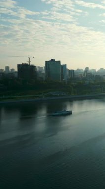 Gün batımında sakin bir nehirde, arka planda şehir manzarası olan beyaz ve mavi yolcu feribotu. Kırp