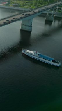 Arabalar gün batımında köprüden geçiyor ve yolcu feribotu nehri geçiyor. Kırp