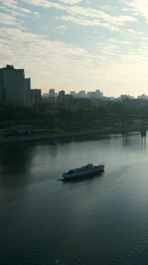 Bulutlu gökyüzünün altında sakin nehirde yol alan beyaz yolcu feribotu. Kırp