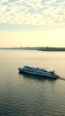 Bulutlu gökyüzünün altında sakin nehirde yol alan beyaz yolcu feribotu. Kırp