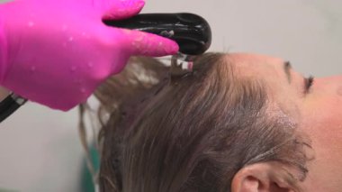 Beyaz tenli müşteri başı, el bilgisayarı spreyiyle durulandı, stilist pembe eldivenli, su akıntısını kontrol etti. Medya