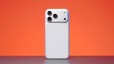 Tiflis, Gürcistan - Eylül 2025: Turuncu arkaplan üzerinde dönen yeni bir kamera tasarımı ile fütürist gümüş cep telefonu. Eylem