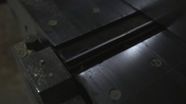 Merkezi tutkal ve cıvata delikleriyle metal masa yerleştirme, ince yansımalar, talaş parçacıkları ve aşınmış atölye. Medya