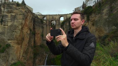 Canyon Köprüsü 'ndeki Adam, Cliff Edge' den Smartphone ile manzara fotoğrafı çekiyor, Tarihi Taş Kemer. Eylem