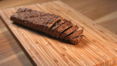 Bambu kesme tahtasının üzerine taze dilimlenmiş tahıllı ekmek serpilmiş susam tohumları. Medya