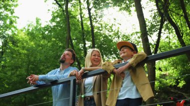 Ağaç tepesini işaret eden üç arkadaş ahşap korkuluklarda kuş izleme, canlı jestler ve paylaşılan şeyler. Kırp