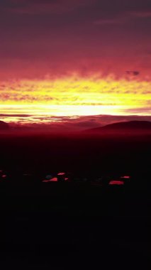 Vadi ışıkları ve sisli bir dağ sırasının üzerinde renkli bir gökyüzü oluşturan canlı bir gün doğumu. Medya