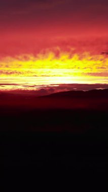 Renkli kırmızı ve sarı gündoğumu karanlık bir dağ manzarası üzerinde bulutları aydınlatıyor. Medya