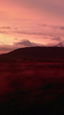 Sisli volkanik bir manzaranın üzerinde güzel mor ve pembe bir günbatımı gökyüzünün havadan görünüşü. Medya