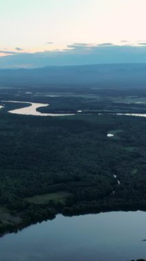 Ufukta dolambaçlı bir nehir, sık bir orman ve dağlar barındıran engin bir doğal manzara. Medya