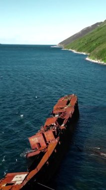 Uzak bir körfez kıyısındaki paslı bir gemi enkazının üzerinde uçan hava aracı. Medya