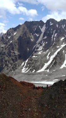 Karla kaplı uzak tepeler ve kayalık ön planlar ile panoramik tepe, trekker bakış açısı engin görüntüler yakalıyor. Medya