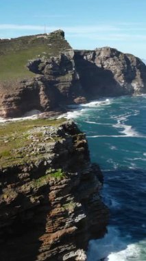 Güneşli burunlar, gök mavisi körfezin yukarısındaki sarmal uçurum yolu, çimenli çıkıntılar ve kayalık kayalıklar ışıldıyor.