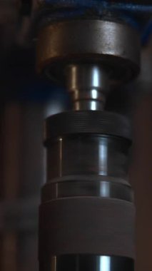 Metal matkap darbesinin tozlu bir atölye ortamında dikey hareket edişinin yakın görüntüsü. Medya