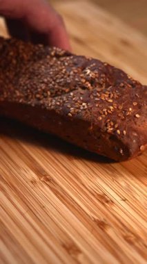 Erkek el, bambu kesme tahtasına susam tohumlu tam tahıllı bir ekmek yerleştiriyor. Medya