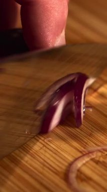 Bambu kesme tahtasındaki taze kırmızı soğanı dilimlemek için bıçak kullanan bir aşçının ellerini kapatın. Medya