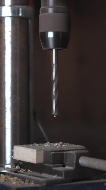 Luthier, bir atölyenin içindeki tahta blokta delik açmak için bir bank matkabı kullanıyor. Medya