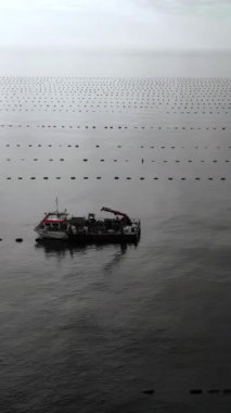 Şamandıra hatları arasında bakım botu, çapaları ve ağları denetleyen mürettebat, yumuşak düşük ışık, geniş sakin deniz,