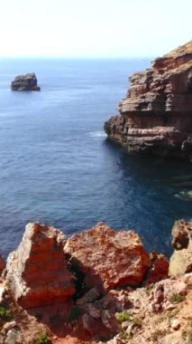 Derin mavi okyanusun yanında kayalık çıkıntılı ve dalgalı, dokulu kızıl kayalıklar ve kıyı şeridi olan yüksek deniz yığını.