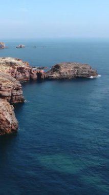 Güneşli kırmızı kumtaşı kayalıkları berrak kıyı deniziyle buluşuyor, koyu mavi kayalar ve koyu mavi kayalar arasında canlı bir zıtlık var.